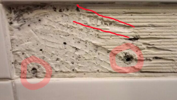 Närbild av vägg med två markerade hål och märken efter fixborttagning, troligen skapat med ett brett verktyg.