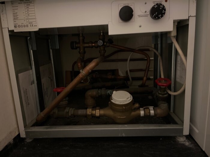 Värmesystem med rör och ventil under en vattenvärmare i ett hus.
