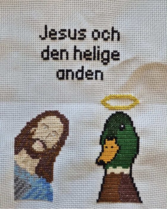 Broderi av Jesus och en and, texten "Jesus och den helige anden" står ovanför, med en gul gloria över anden.