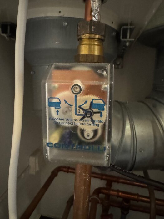 Kopplingsbox på kopparrör med instruktionen "Disconnect before turning" och några inristade symboler i ett tekniskt utrymme.
