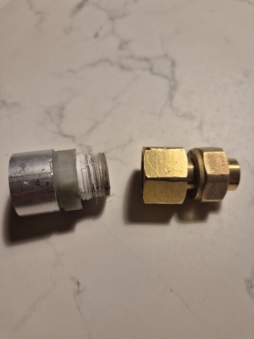 Två kopplingar, en med vita gummidetaljer och en i mässing, placerade på ett bord.