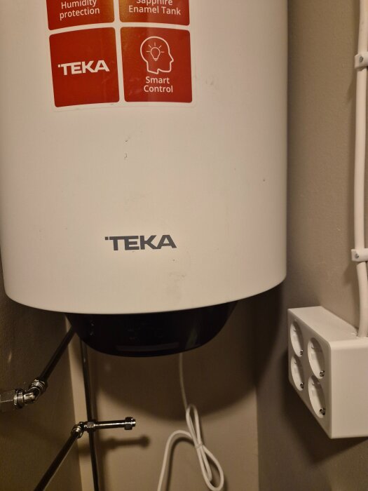 Varmvattenberedare från Teka med smart kontrollfunktion, monterad på vägg bredvid ett eluttag med fyra uttag.