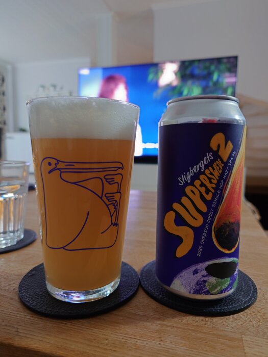 Ett glas öl och en burk med etiketten "Superswede 2" står på ett bord framför en tv.