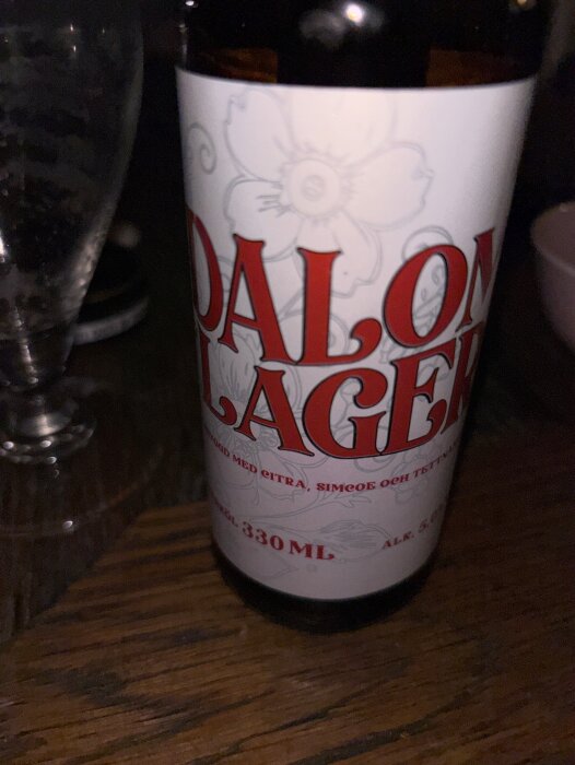 Flaska med Dalom Lager öl på ett träbord, bredvid ett halvtomt glas.