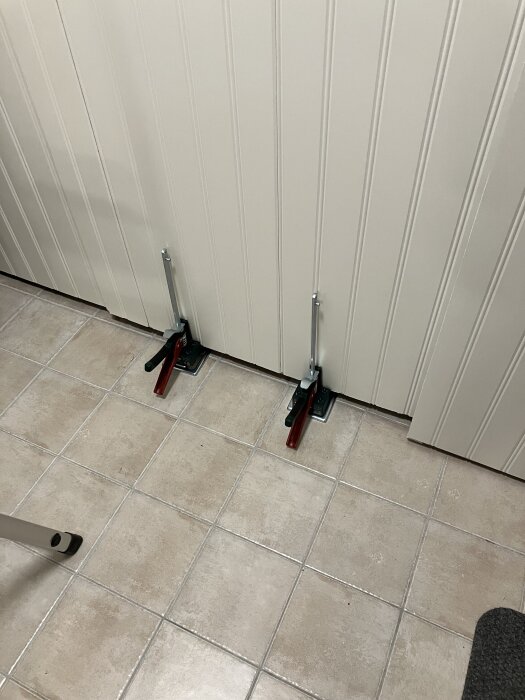 Två golvlyftar i bruk för att installera eller justera skivor av väggpanel i rum med klinkergolv.