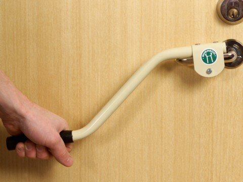 Hand som håller i en vit dörr- och fönsteröppnare fäst på ett dörrhandtag.