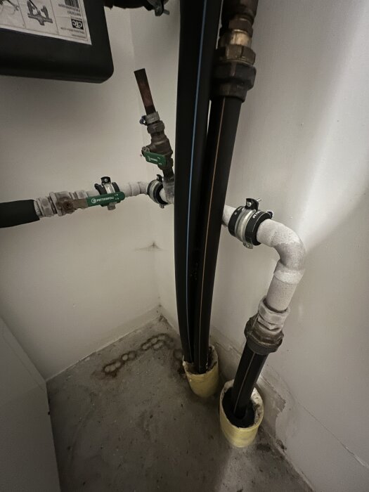 Lödade kopparrör och ventiler i ett köldbärarsystem, delvis isolerade, med tecken på isbildning och fukt vid rörens bas på ett betonggolv.