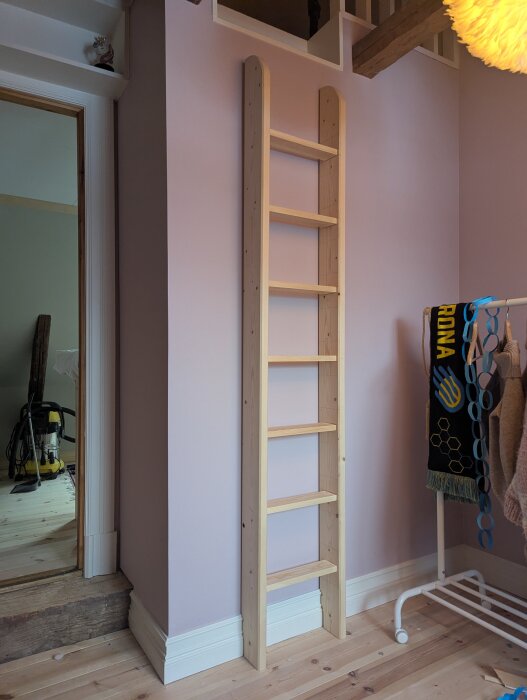 Trästege lutad mot lila vägg, del av sovloft; stegen når inte loftet helt och är tänkt att fästas med vinkeljärn för stabilisering.