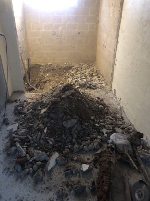 Källarprojekt med bortbilad betong och jord för att förbereda installation av golvvärme. Rester och verktyg ligger på golvet.
