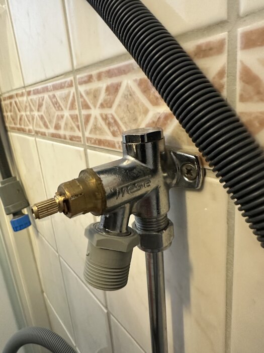 VVS-komponent på kaklad vägg med metallventil och kopplingar, troligen en vattenventil där insatsen/packningen verkar behöva bytas.