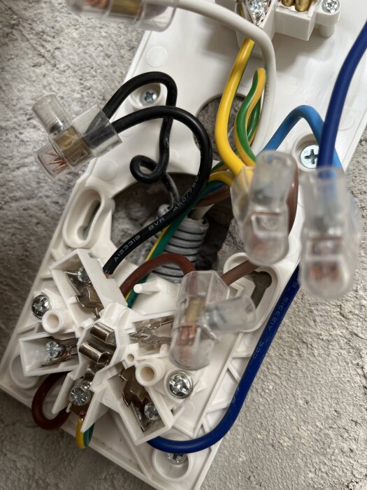 Elinstallation med flera kablar i olika färger, anslutna till ett vägguttag och en kopplingsdosa, visar elektriska ledningar och kontakter.