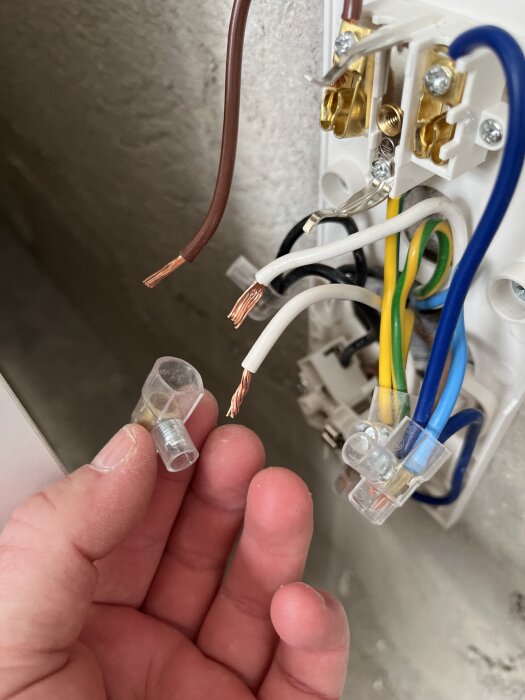 Elektrisk installation med oskyddade koppartrådar och en handenhet som håller en kabelhylsa.