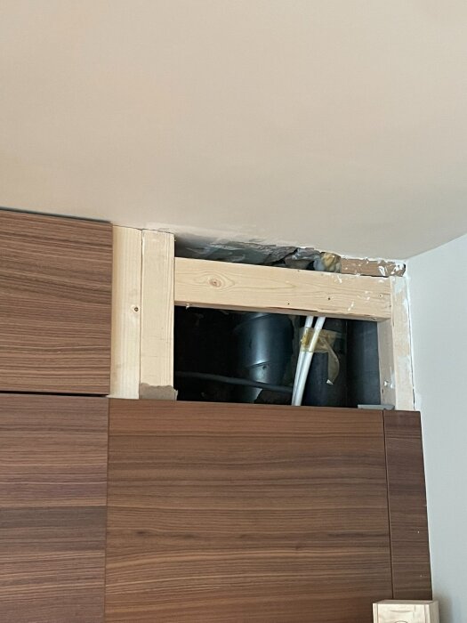 Håltagning i väggen ovanför köksskåp med synliga ventilationsrör och träkonstruktion för frånluftskoppling i köket.
