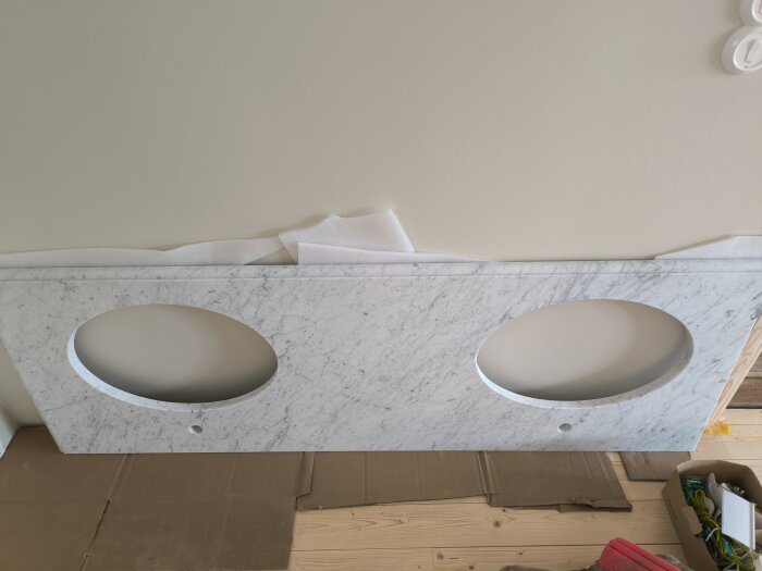 Marmorskiva med två utskärningar för handfat ligger på kartong på golv, förberedd för installation på en kommod.