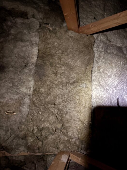 Blöt isolering och träreglar på vinden, orsak vid murstocken i ett hus byggt 1965, möjligt kondensproblem.