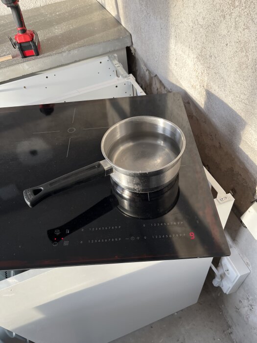 Kasstro med vatten på en induktionshäll med borrmaskin i bakgrunden, del av ett renoveringsprojekt.