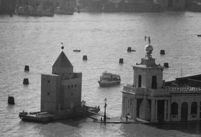 Svartvitt foto av Aldo Rossis flottande Teatro del Mondo i Venedig, omgivet av vatten och båtar.
