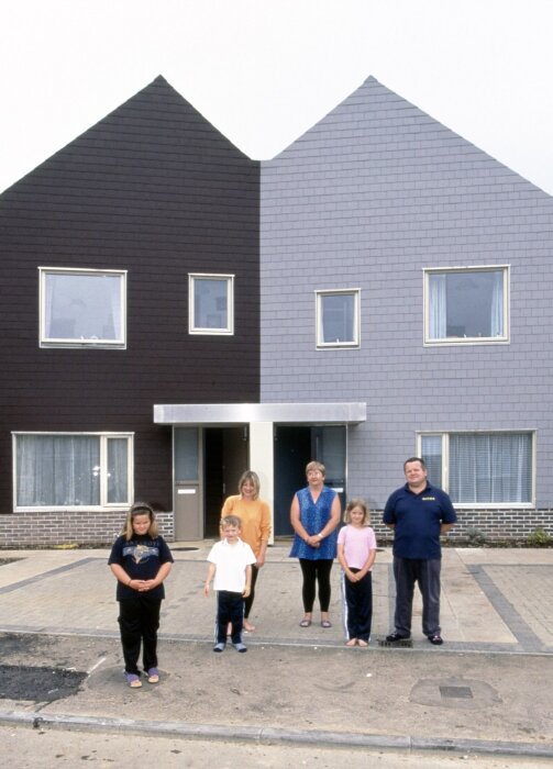 En grupp människor framför tvåfärgat hus, med halva fasaden i mörkt grått och den andra i ljusgrått.