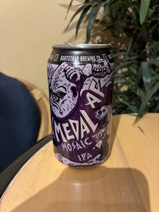 En burk Bootstrap Brewing Co. Medal Mosaic West Coast IPA med tecknad gorilladesign står på ett bord.