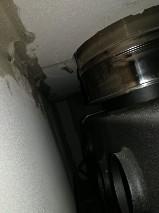 Ventilationsrör och fläktkonstruktion, delvis installerad i ett trångt utrymme, med rostfritt stål och svarta element.