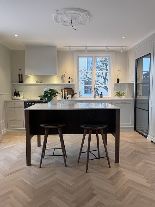 Modernt kök med ljusa trägolv, köksö, två barstolar och marockansk stukatur i taket, dekorativt fönster och minimalistic inredning.