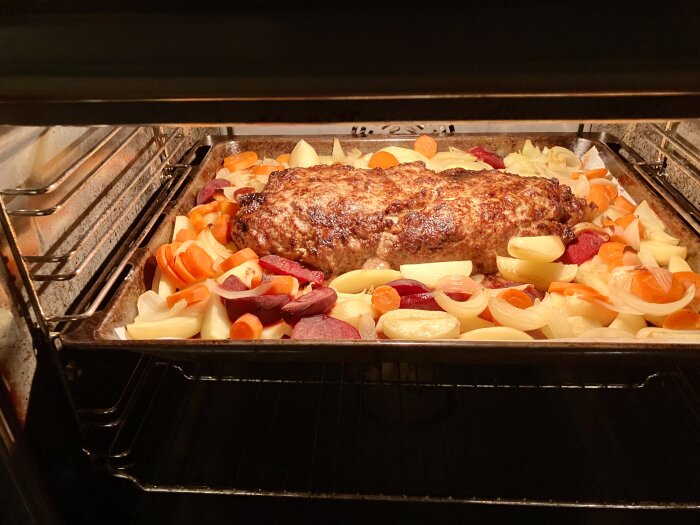 Köttfärslimpa i ugn med morötter, lök, potatis och rödbetor på en plåt.