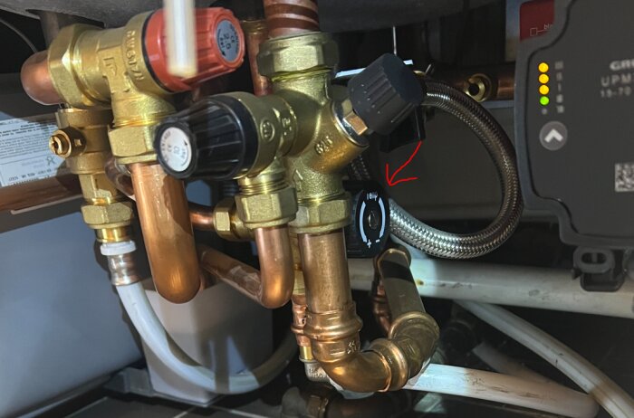 VVS-installation med kopparrör och kopplingar under en diskbänk, med en märkning på en ratt markerad i rött.