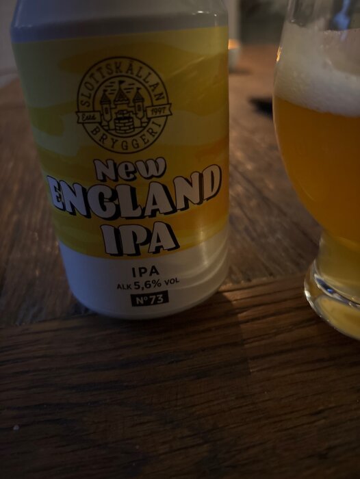 En burk New England IPA från Slottskällans bryggeri och ett glas häller upp med öl på ett träbord.