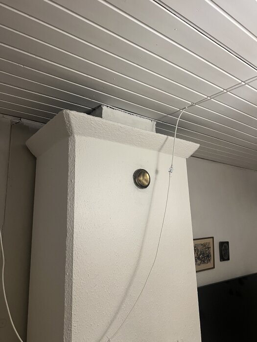 Murstock i taket av ett 70-tals kedjehus. Vitmålad struktur med koppling och kabel synlig. Tak med svag lutning och vit innertakspanel.