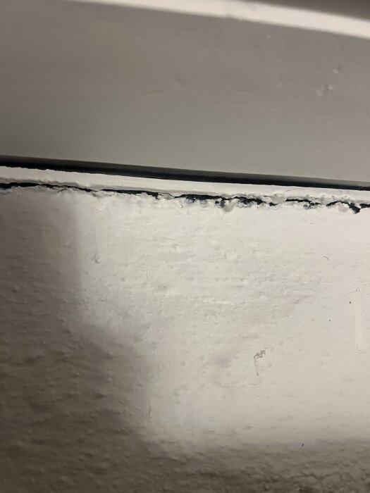 Närbild av en vit vägg och takkant med synlig spricka eller fog, potentiellt otätt område i ett 70-talshus.