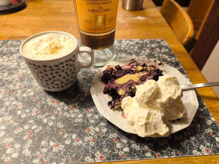 Blåbärspaj med grädde på en tallrik bredvid en mugg med Irish coffee, stående på ett bord med en flaska whisky i bakgrunden.