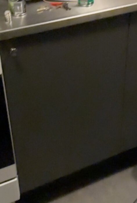 Grå köksbänk med mörka skåpluckor och en rostfri bänkskiva. Ovanpå ligger verktyg och burkar placerade.