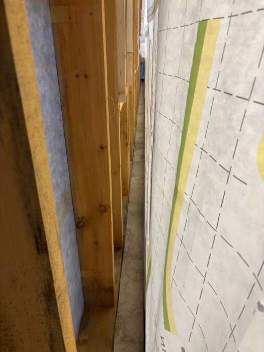 Närbild på en byggvägg med träreglar och ångbromsfilm, fokuserar på installationsdetaljer och tejpning mellan reglarna.
