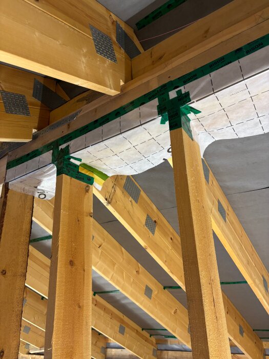 Välbyggd takstomme med synliga träbjälkar och grön tejp för ångbroms, uppsatt på byggplats under installation av lösullsisolering.