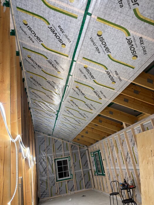 Isolering och ångbroms installerad i tak och väggar i ett träinramat rum under byggnation, med exponerat träarbete och plywood.