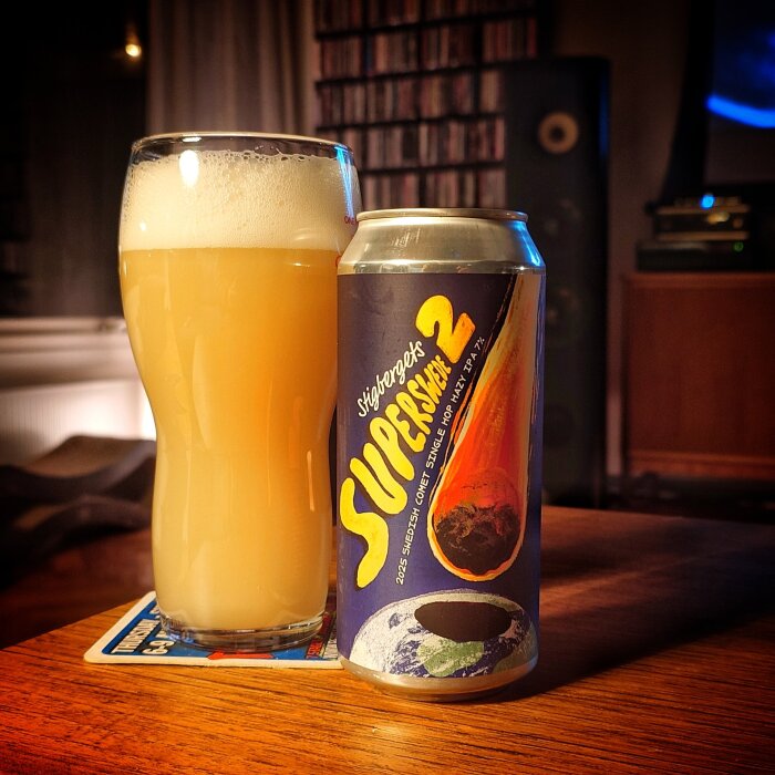 Ett glas fyllt med ljus öl bredvid en burk med etikett märkt "SUPERSWEE" står på ett bord i ett vardagsrum.