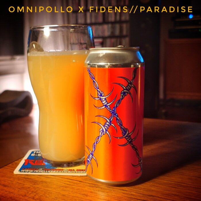 Dryck i ett glas bredvid en burk med orange och blå design, står på ett bord.