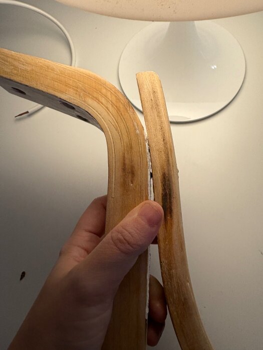 Hand håller två trädelar av en stol med märken och övermålad skruv.