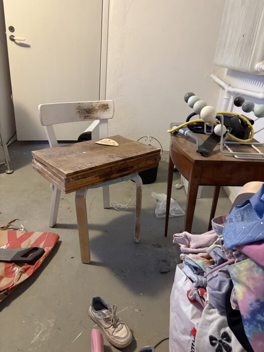 Sliten trästol under renovering i ett rum, omgiven av verktyg och tyg.
