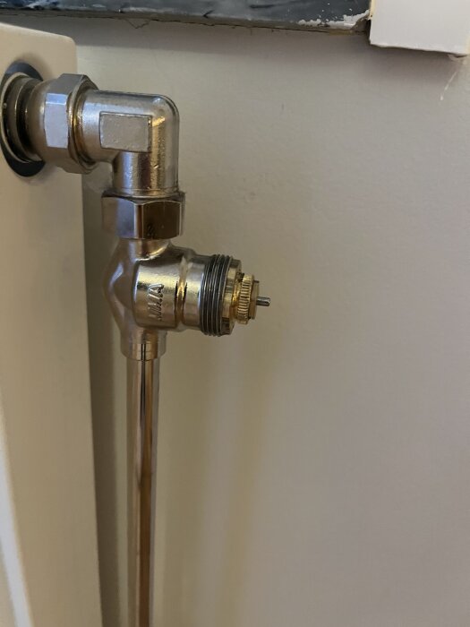 Radiatorkoppling med Purmo/MMA-märkt fördelare och insexnyckelspår, synlig spindel ovanför termostatanslutning, monterad på vägg.