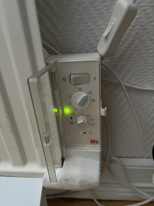 Termostat på element med grönt ljus, knappar inställda på olika temperatur- och lägen.