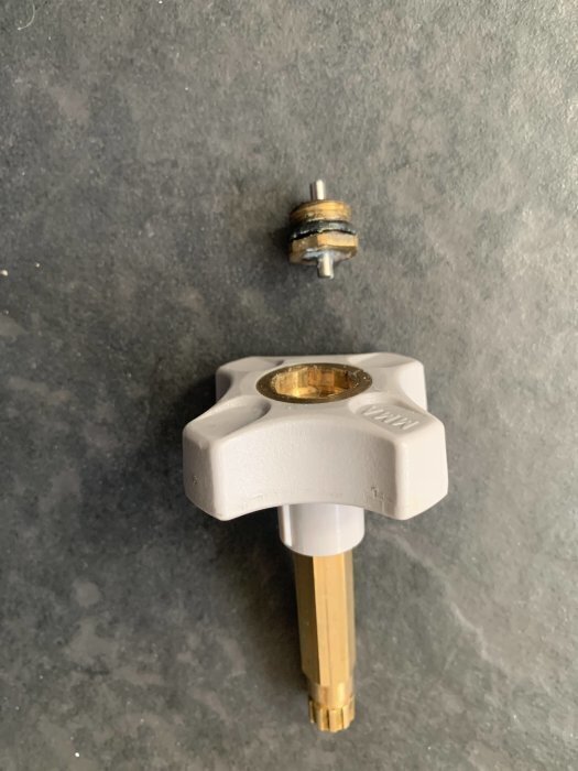 Radiatorventil med grått handtag och borttagen packbox placerad ovanpå en grå yta.