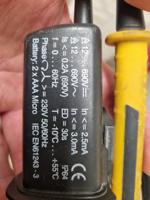 Närbild av en elektrisk komponent med tekniska specifikationer och symboler tryckta på ytan, inklusive information om spänning och batterityp.