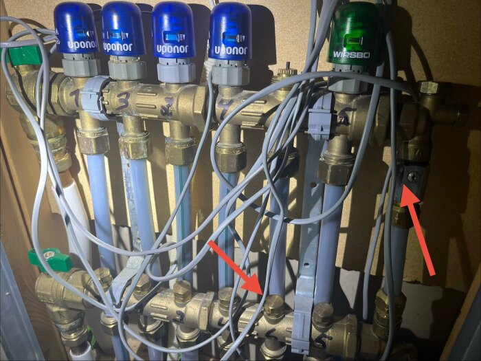 Uponor golvvärmesystem med ställdon och rör. Två röda pilar pekar på potentiella justeringspunkter för flödet i systemet.