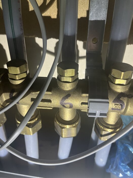 Golvvärmesystem med flera rör och ventiler, nära bild av komponenter märkta med siffror, del av diskussion om problem med golvvärme i badrum.