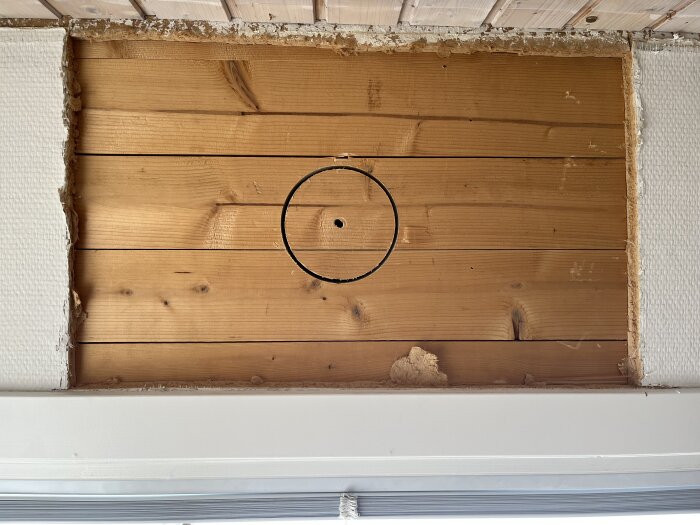 Cirkulärt märke på träpanel i ett vägguttag med frilagd panel från ett hus byggt 1944, förberett för ventilationsinstallation.