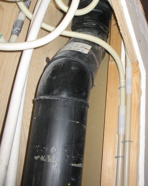 Svart ventilationsrör från byggår 1978-79 i ett trätak med vita slangar runtom.