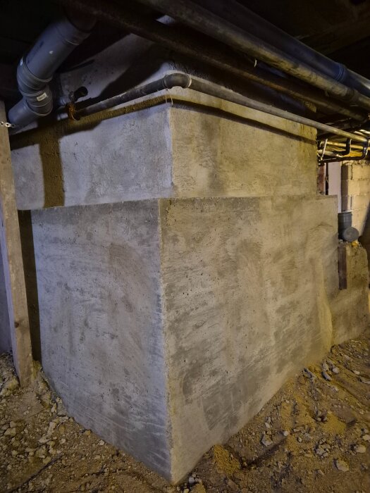 Betongfundament med rör och ledningar monterade ovanpå, omgiven av grus i en underjordisk miljö.