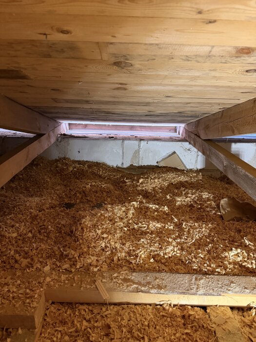 Ett loftutrymme med träram och sågspån på golvet, med fokus på en yta där vindavledaren ska installeras mot en stenmur.