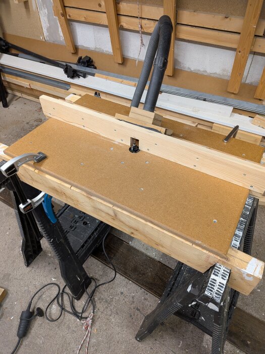 Hembyggt fräsbord med träanhåll och dammsugarslang i en verkstad, för att avsluta projekt.